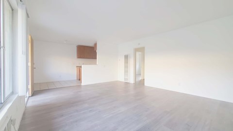 A room with white walls and wooden flooring with a window on the left.