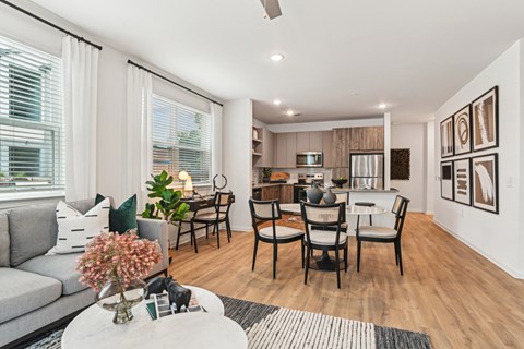 A modern living room with a grey sofa, a coffee table, and a dining table set up with chairs.