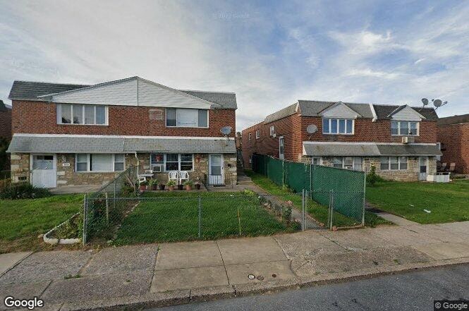 A street view of a residential area with houses and a green fence.