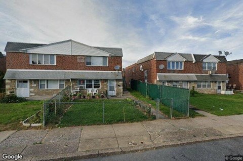 A street view of a residential area with houses and a green fence.