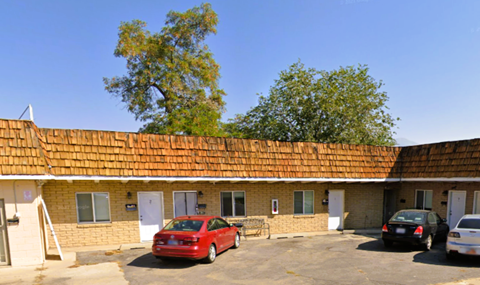 A red car is parked in a lot in front of a building with a brown roof.