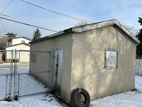 A small concrete building with a tire leaning against it in the snow.