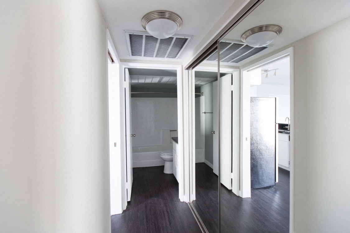 a hallway with white walls and a toilet and a mirror