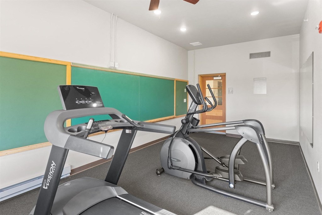 a fitness center with cardio machines, wall chalkboards and a mirror