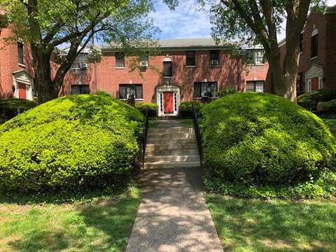 A red brick building with a red door and two green bushes on either side.