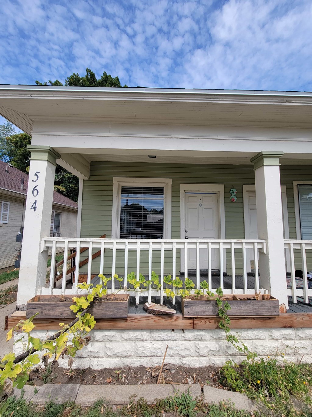 the front porch of a green house with a white railing