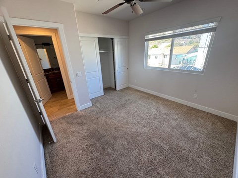 A room with a carpeted floor and a window showing a view of a pool and houses outside.