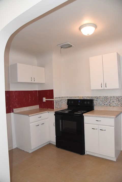 an empty kitchen with white cabinets and a black stove
