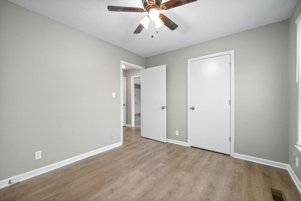 an empty living room with a ceiling fan and a door to a hallway
