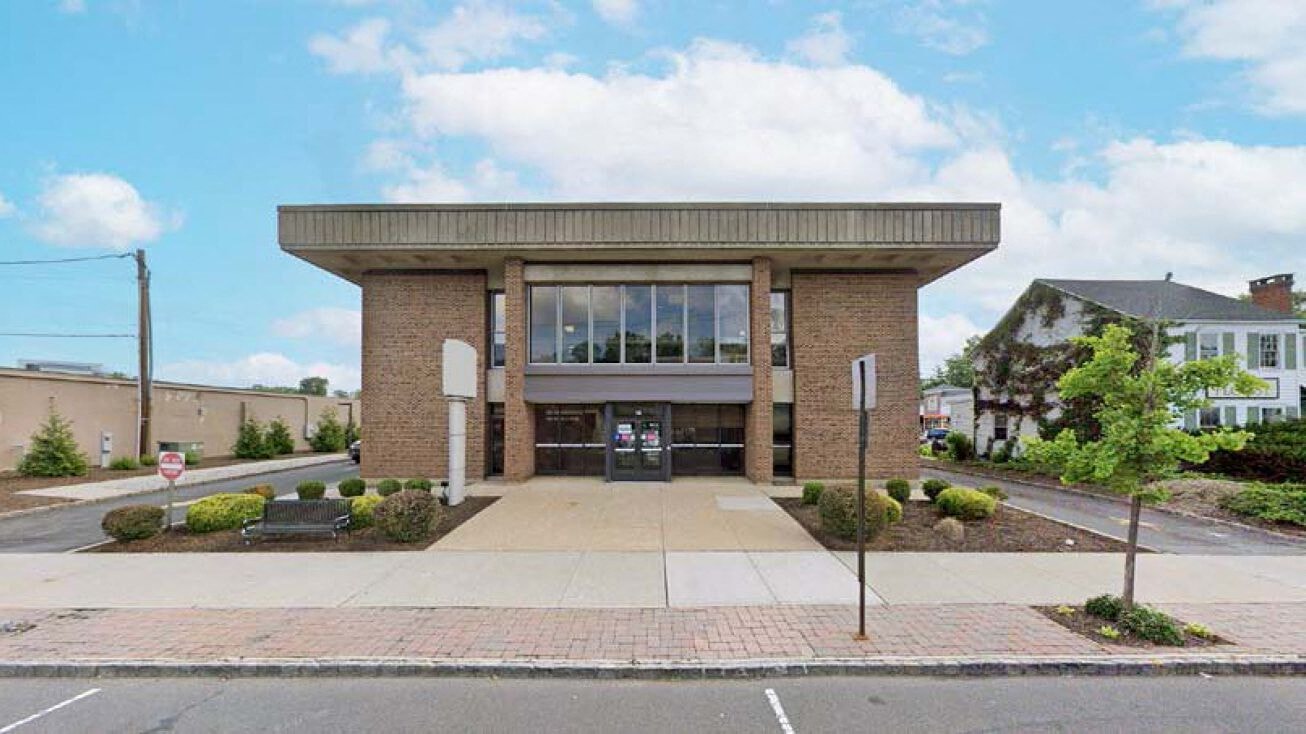A small building with a brick facade and a glass door is surrounded by a brick walkway.