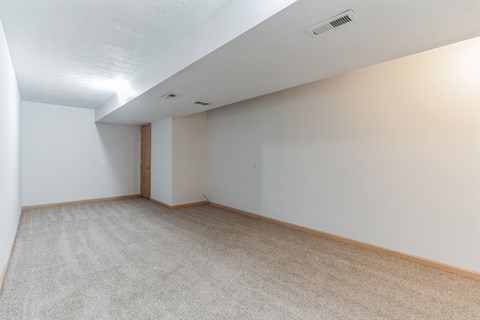 the living room and dining room of an apartment with white walls and carpet