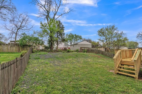the backyard of a house with a fence and a lawn and a bench