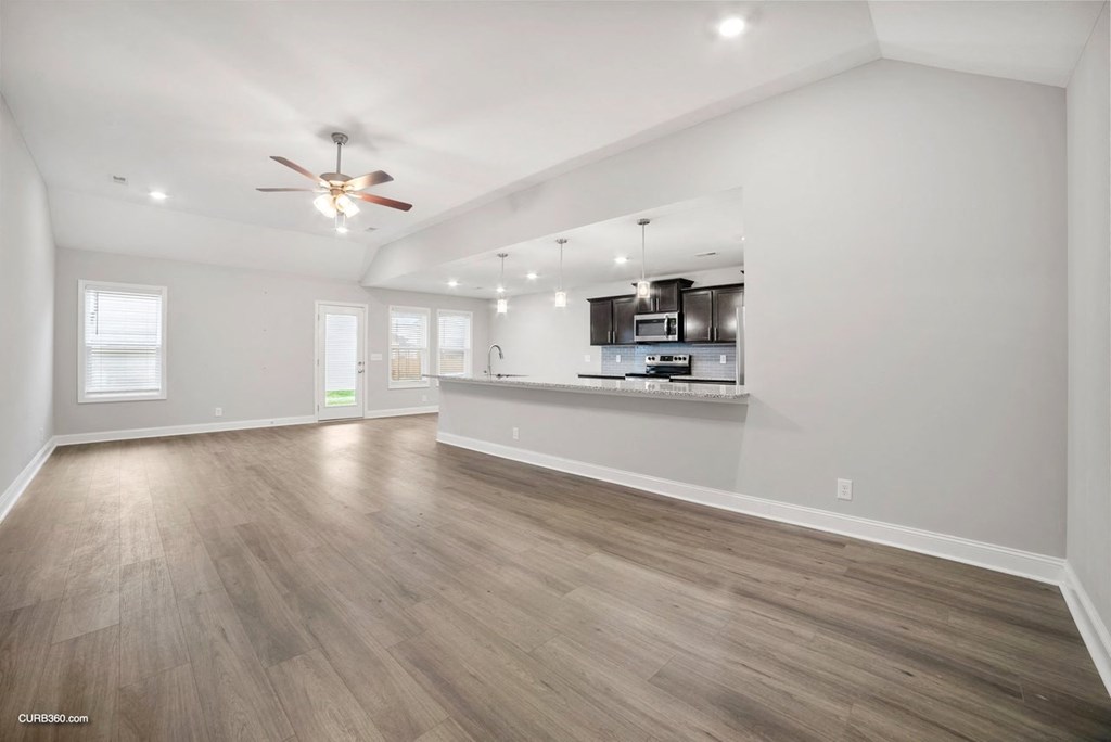 an empty living room with a kitchen and a ceiling fan