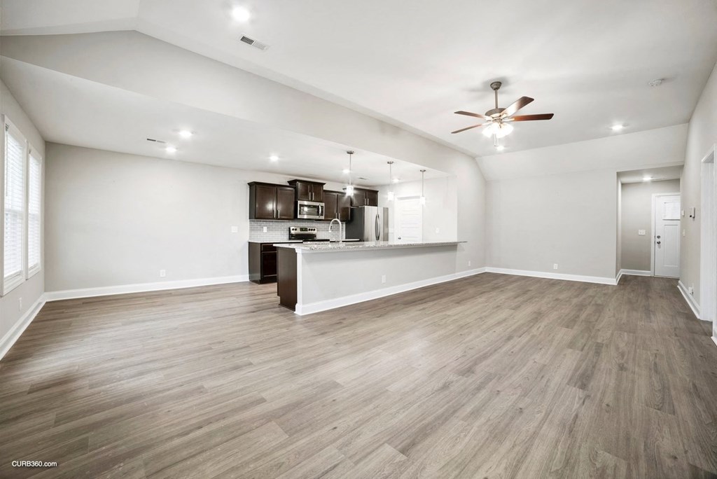 an empty living room with a kitchen and a ceiling fan
