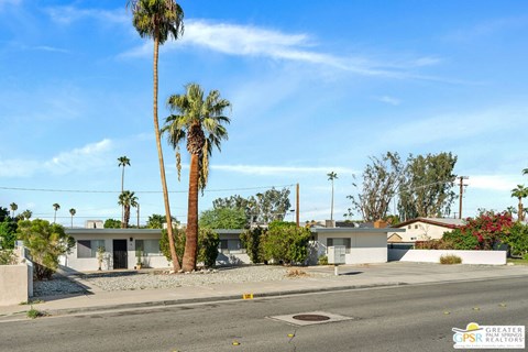 an empty street in front of a house with palm trees