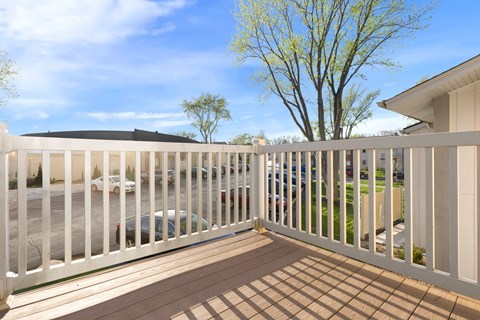 A white fence encloses a patio with a view of a parking lot and trees.