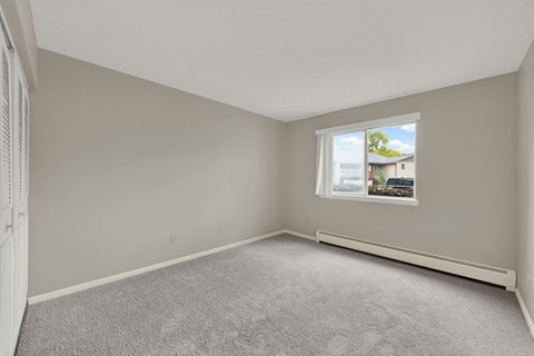 A room with a carpeted floor and a window showing a house and trees outside.