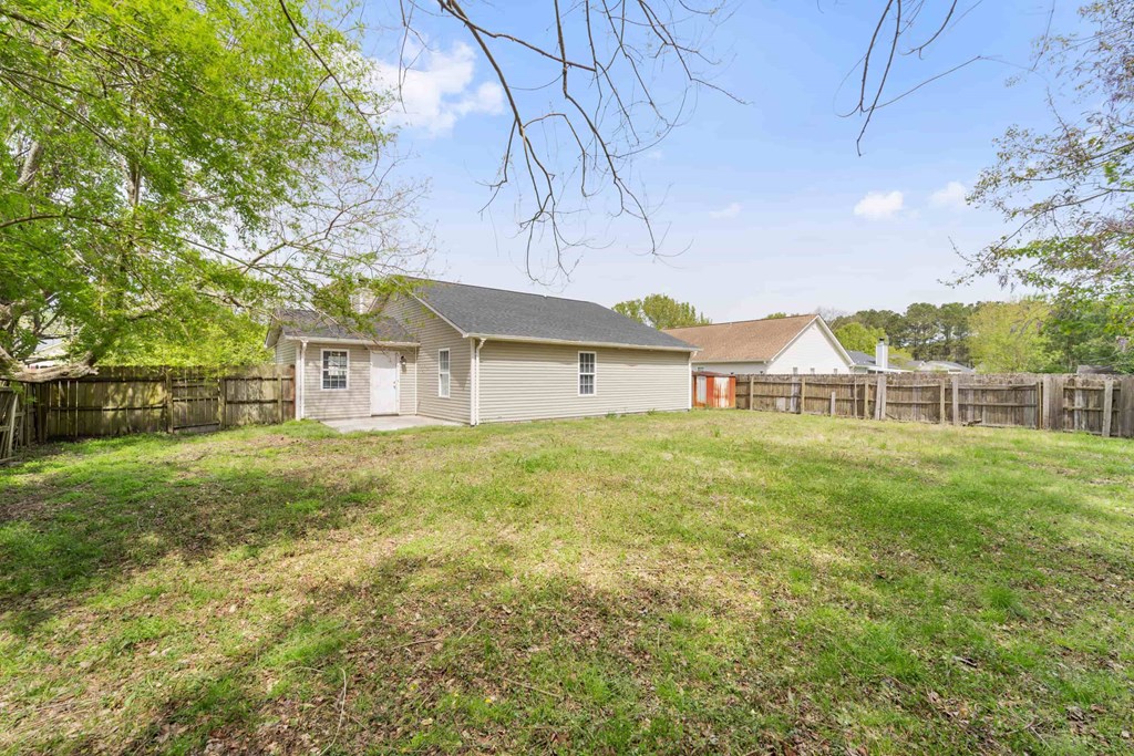 A house with a grey roof and a red door is surrounded by a grassy area and trees.