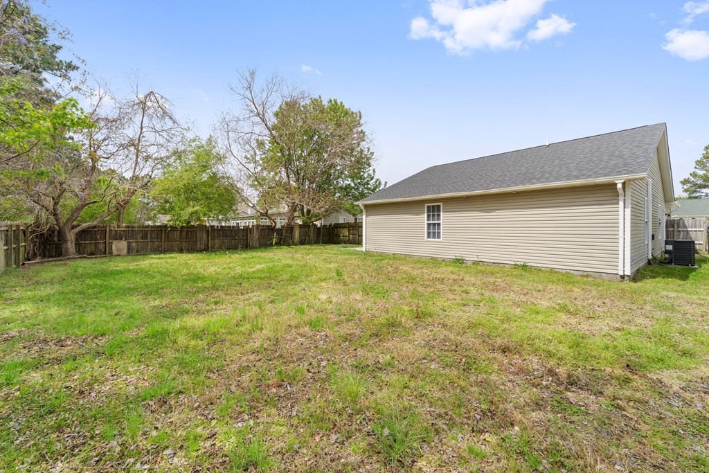 A small house with a grey roof is surrounded by a fence and trees.