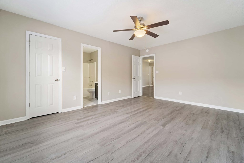 A spacious room with a ceiling fan and light, hardwood floors, and white walls.
