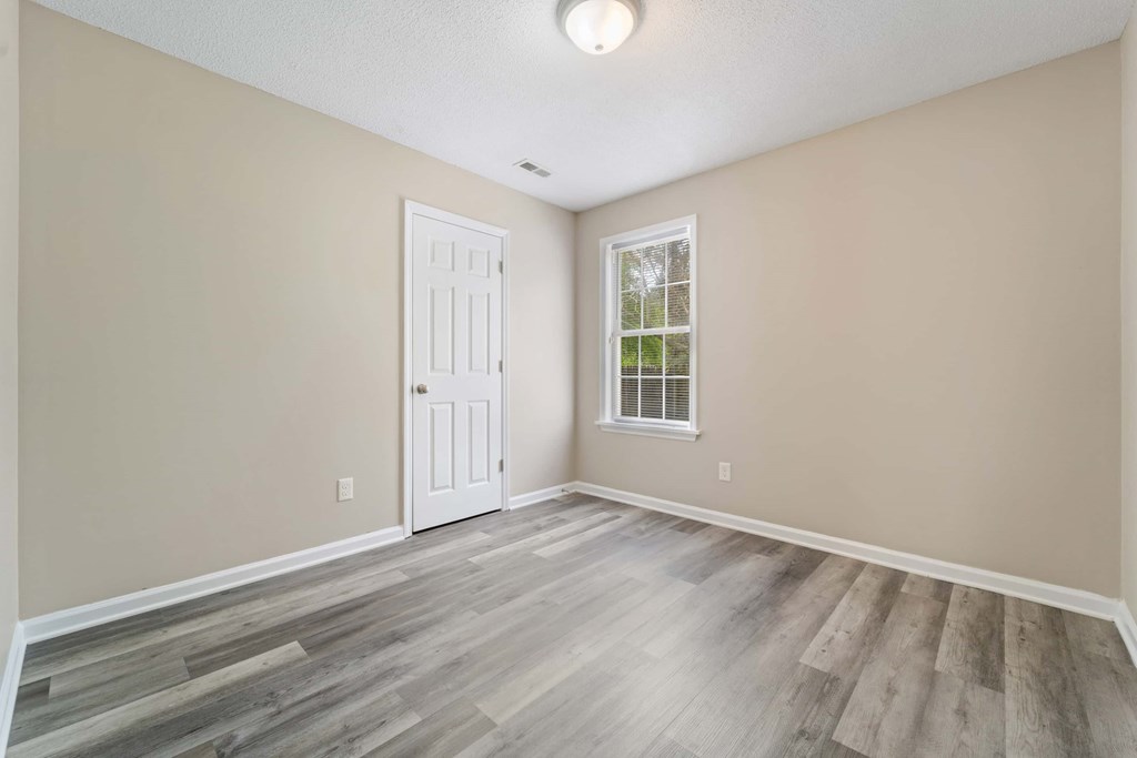 A room with a white door and a window with a view of trees.