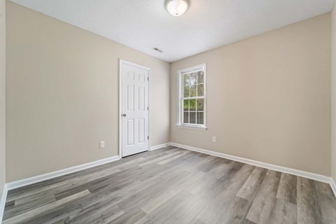 A room with a white door and a window with a view of trees.