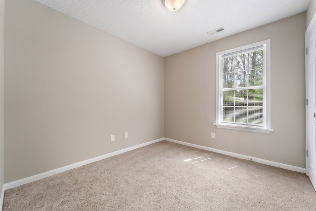 A room with a carpeted floor and a window with blinds.