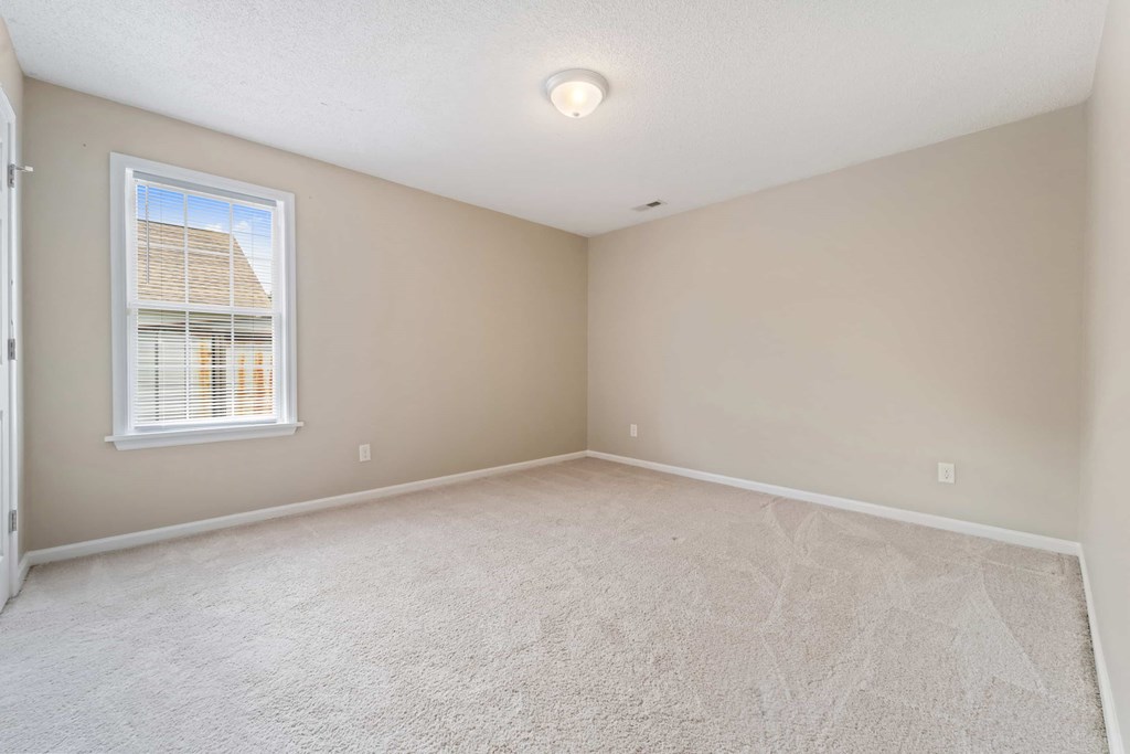 A room with a carpeted floor and a window with blinds.
