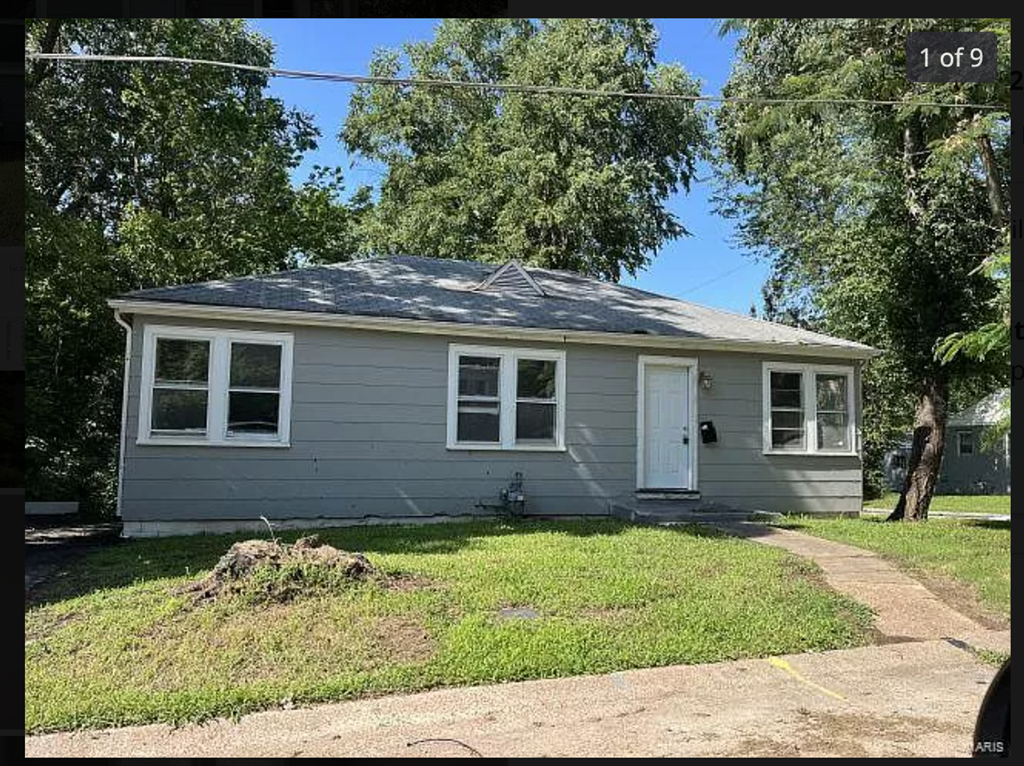 a small gray house with a sidewalk and trees