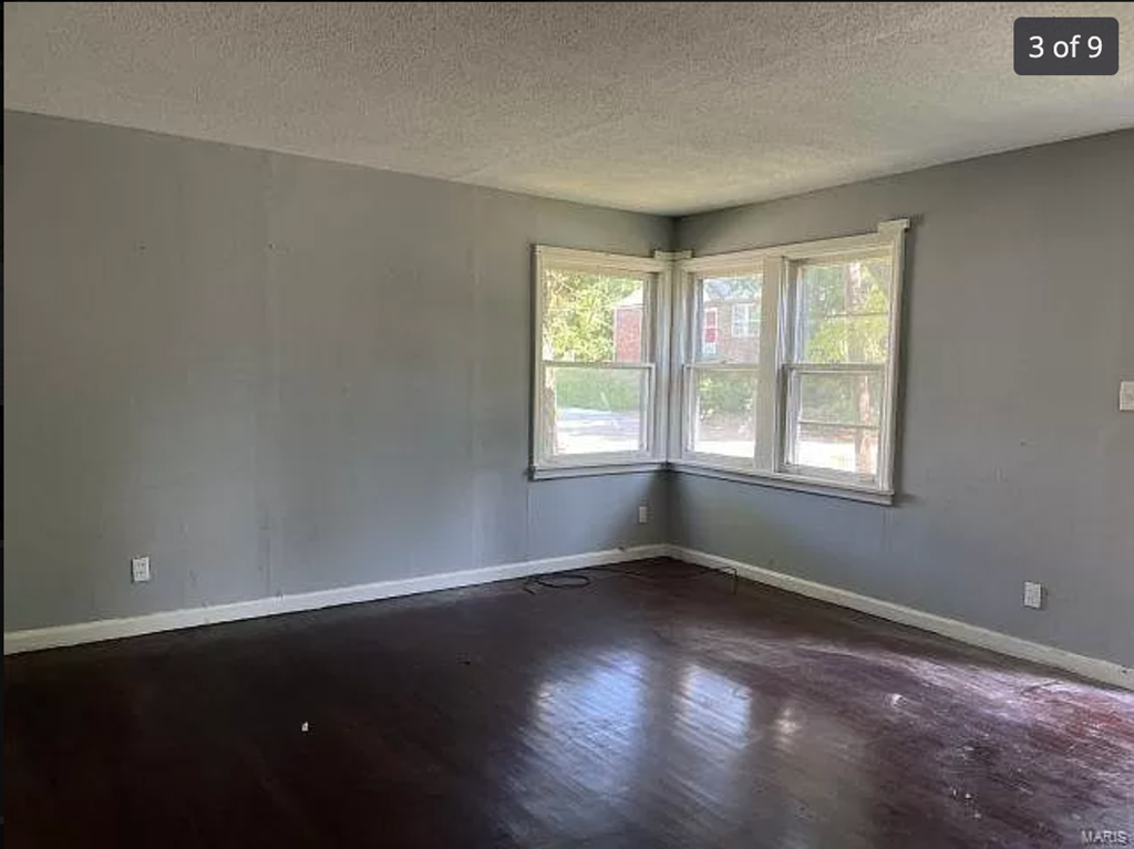 an empty room with a wood floor and three windows