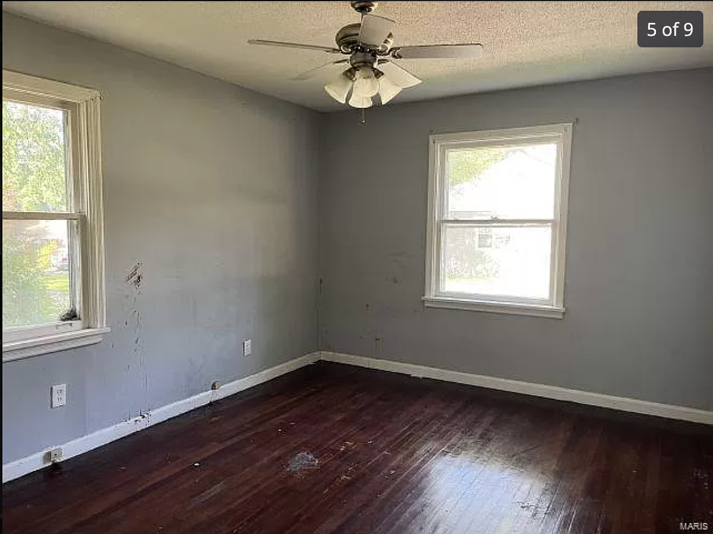 an empty room with a ceiling fan and two windows