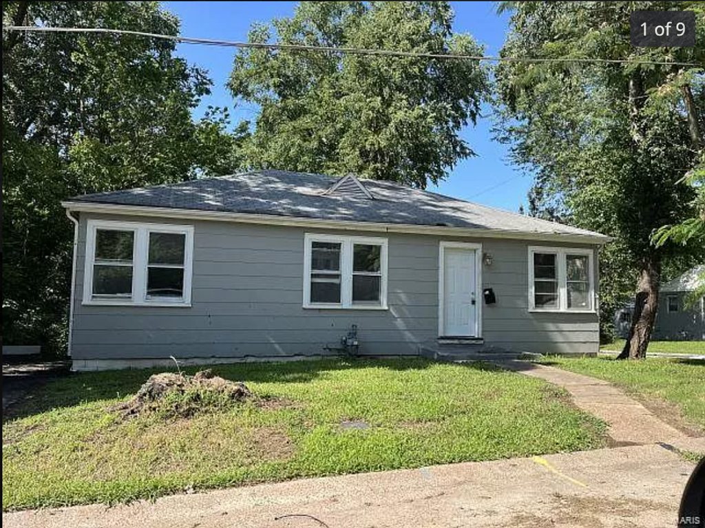 a small gray house with a yard and trees