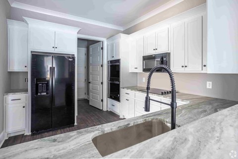 A kitchen with white cabinets and a black fridge.
