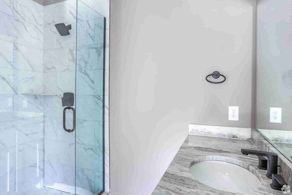A modern bathroom with a glass shower door and a marble countertop.
