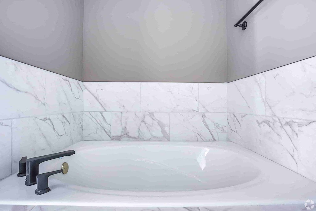A white bathroom with a marble tile wall and a white bathtub.