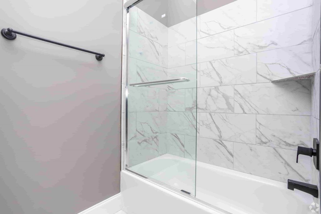 A white bathroom with a marble wall and a glass shower door.