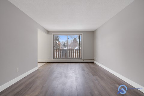 A spacious room with wooden floors and a large window overlooking a balcony.