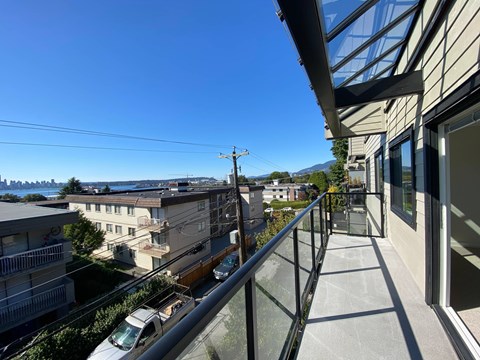 A balcony with a glass railing overlooks a residential street.