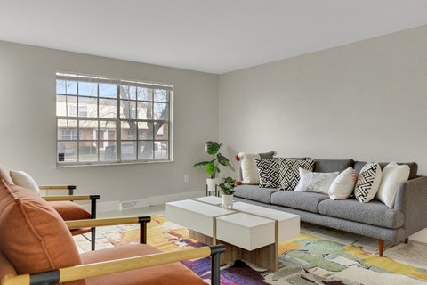 A living room with a grey couch, a white coffee table, and a window with a view of a building.