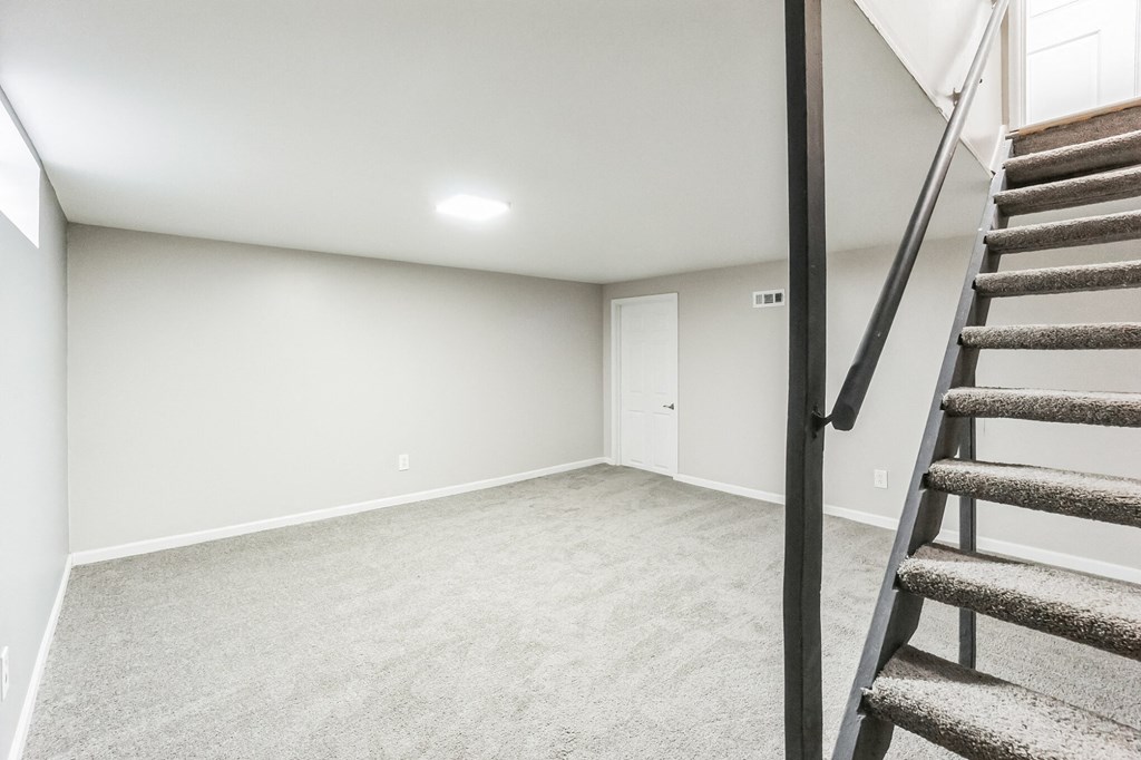 A room with a carpeted floor and a staircase leading to another room.