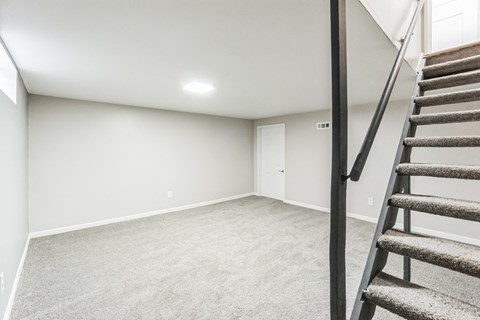 A room with a carpeted floor and a staircase leading to another room.