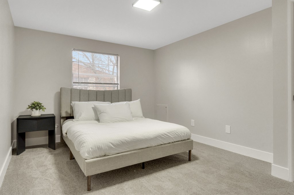 A bedroom with a bed, nightstand, and window.