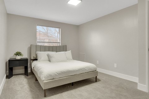 A bedroom with a bed, nightstand, and window.