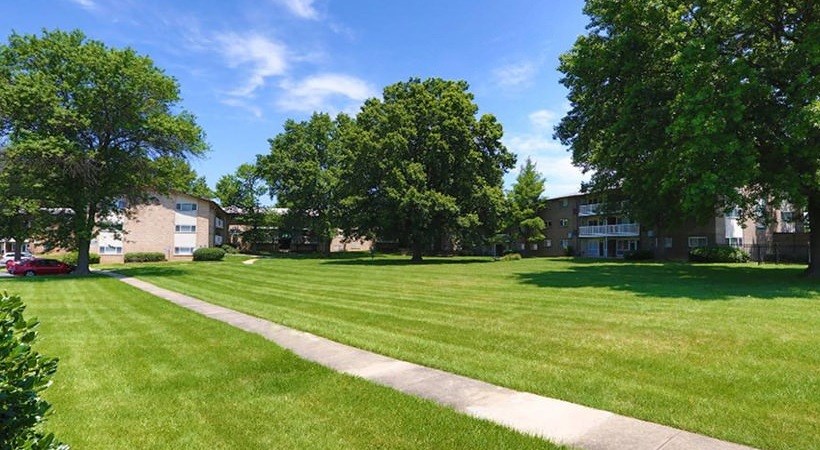 A green lawn with a pathway and trees in front of a building.