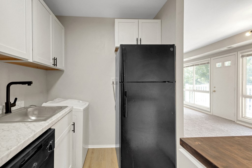 A black refrigerator stands in a kitchen with white cabinets and a marble countertop.