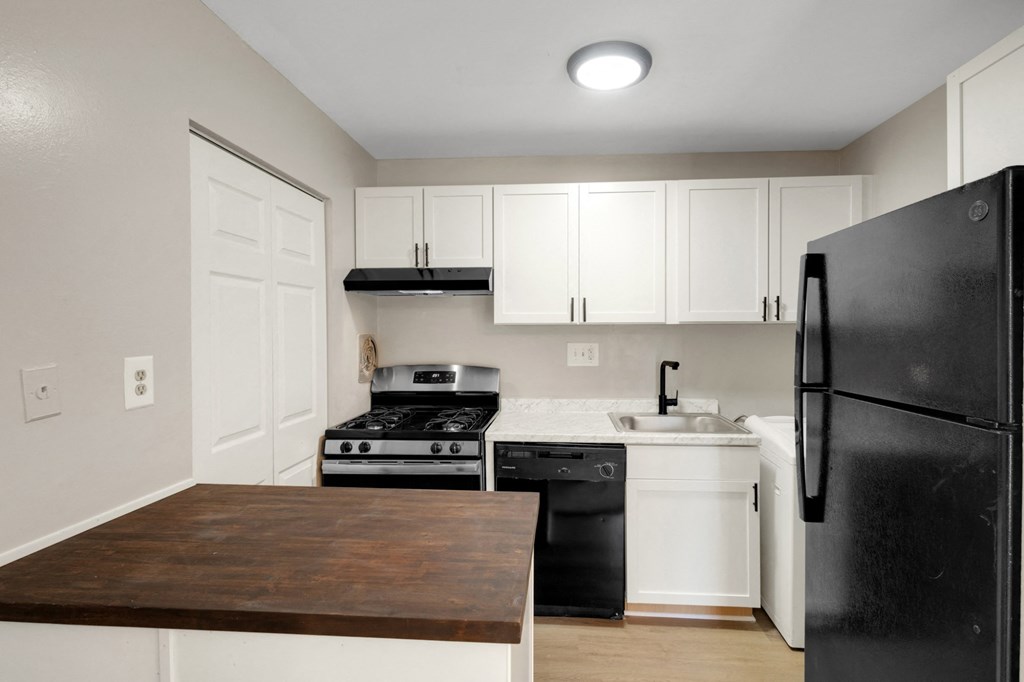 A black refrigerator is in a kitchen with white cabinets.