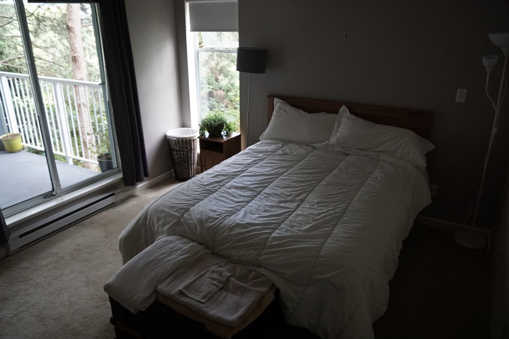 A bed with white sheets and pillows in a room with a window.