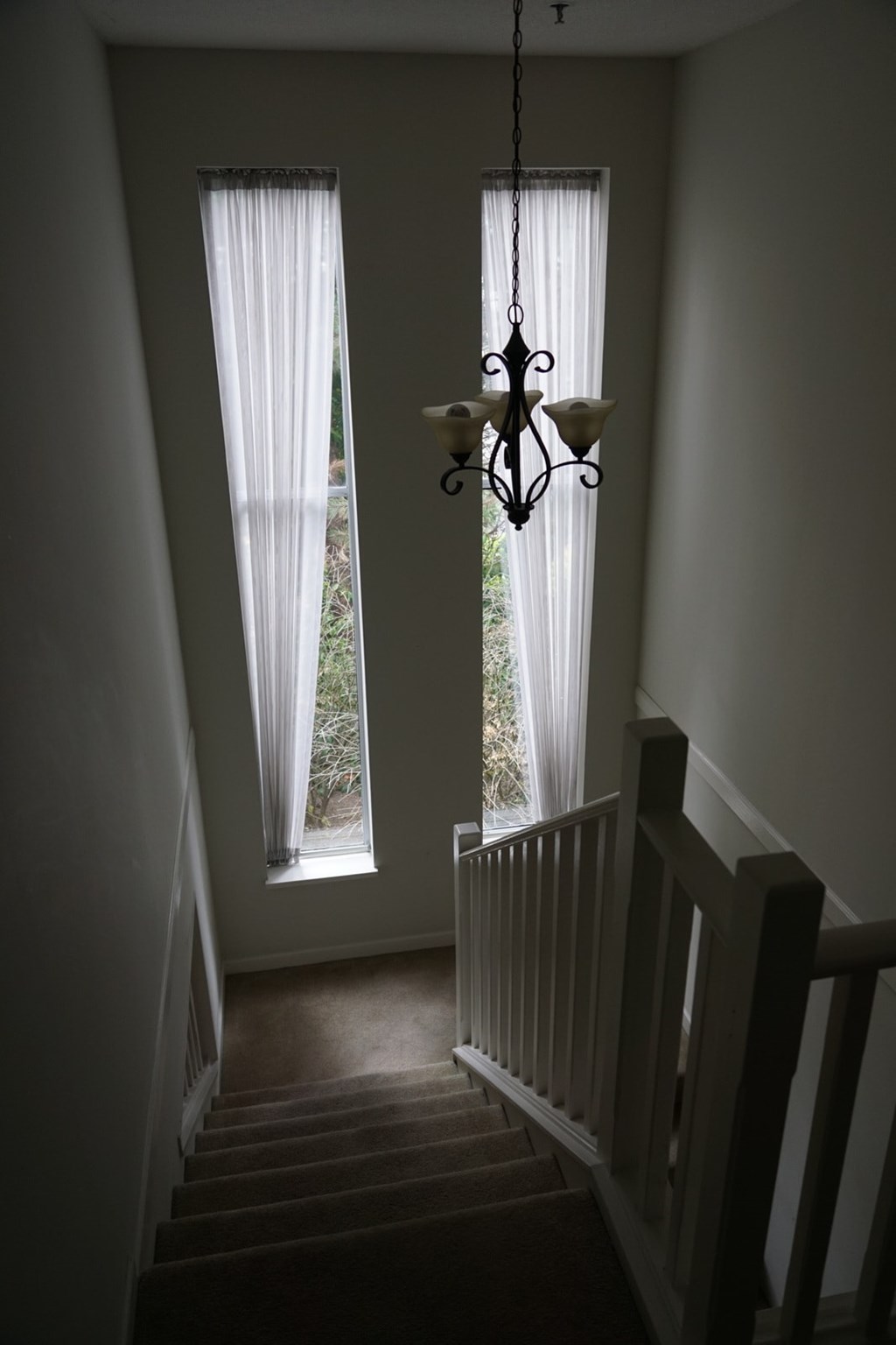 A chandelier hangs over a staircase with a window in the background.