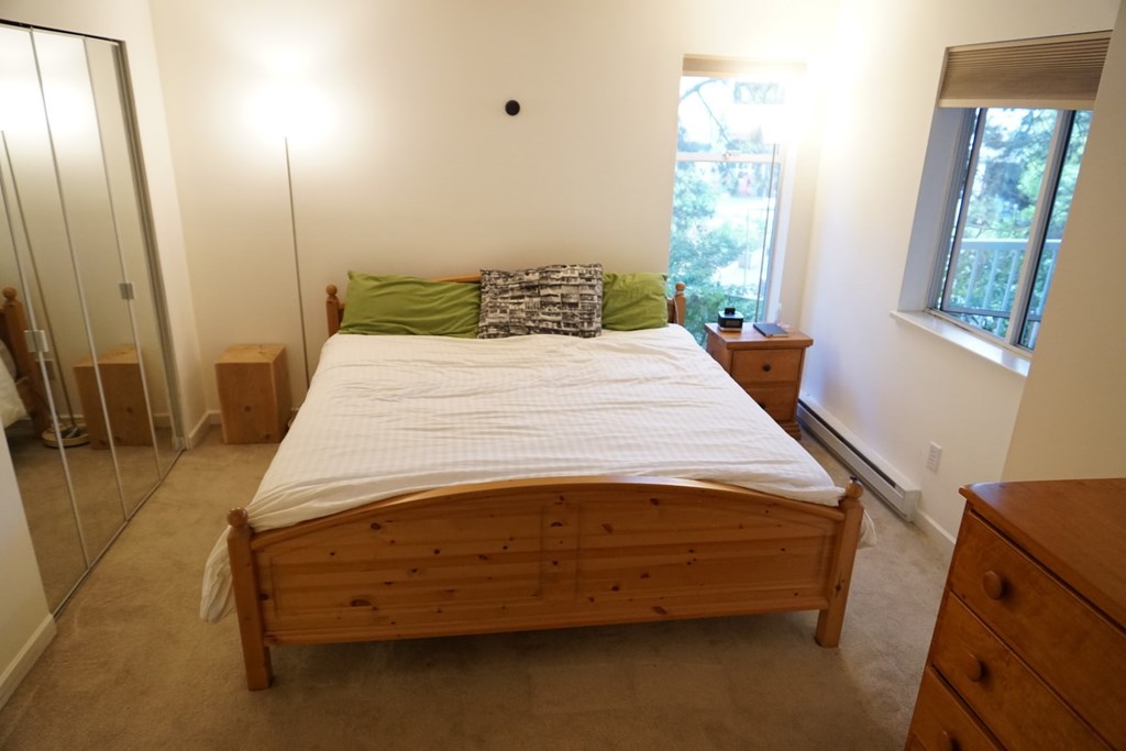 A bedroom with a bed, nightstand, and a window.