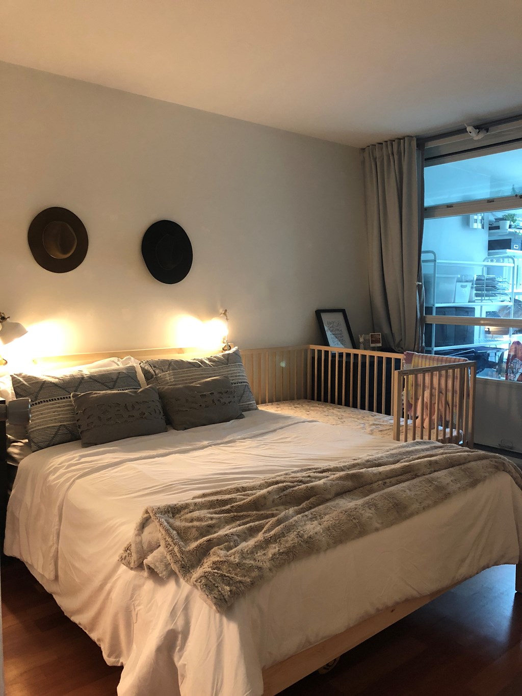 A white bed with a grey blanket and pillows in a room.